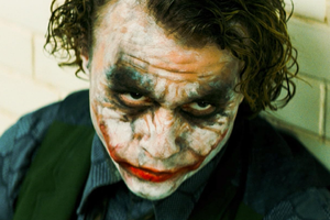 Na zdjęciu Heath Ledger jako Joker - mężczyzna z pobrudzoną twarzą, niebieskimi oczami i kręconymi włosami.
