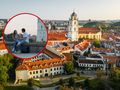 Widok na miasto z parą siedzącą na murku, w tle kościół i dachy budynków.