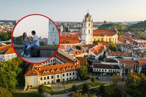 Widok na miasto z parą siedzącą na murku, w tle kościół i dachy budynków.