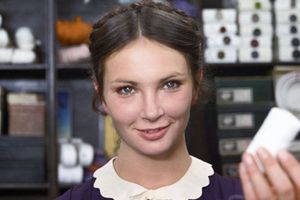 Młoda kobieta trzyma w dłoni mały przedmiot, uśmiechając się w tle z kolorowymi akcesoriami.