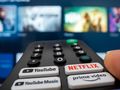 Pilot do telewizora z aktywnym przyciskiem Netflix, w tle wyświetlacz TV.