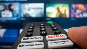 Pilot do telewizora z aktywnym przyciskiem Netflix, w tle wyświetlacz TV.