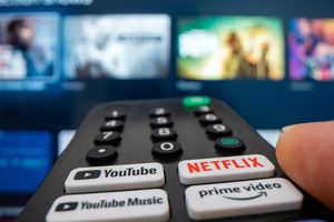 Pilot do telewizora z aktywnym przyciskiem Netflix, w tle wyświetlacz TV.