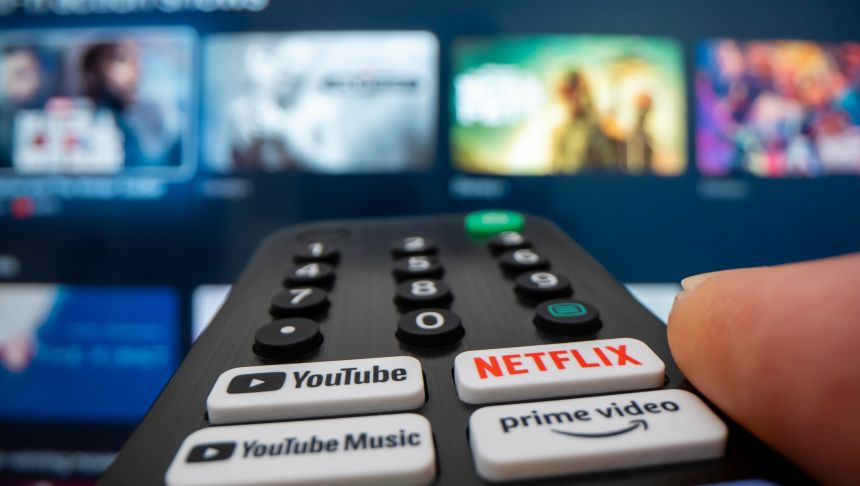 Pilot do telewizora z aktywnym przyciskiem Netflix, w tle wyświetlacz TV.
