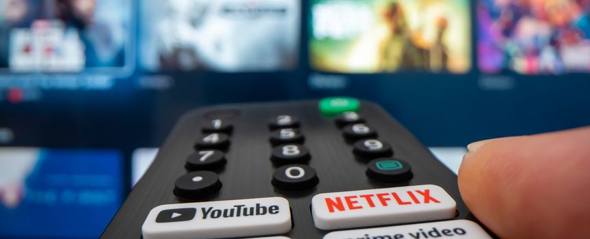 Pilot do telewizora z aktywnym przyciskiem Netflix, w tle wyświetlacz TV.