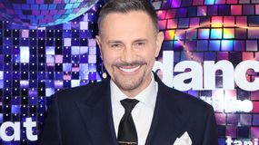 Krzysztof Ibisz w garniturze, uśmiechnięty, na tle kolorowych dyskotekowych luster.