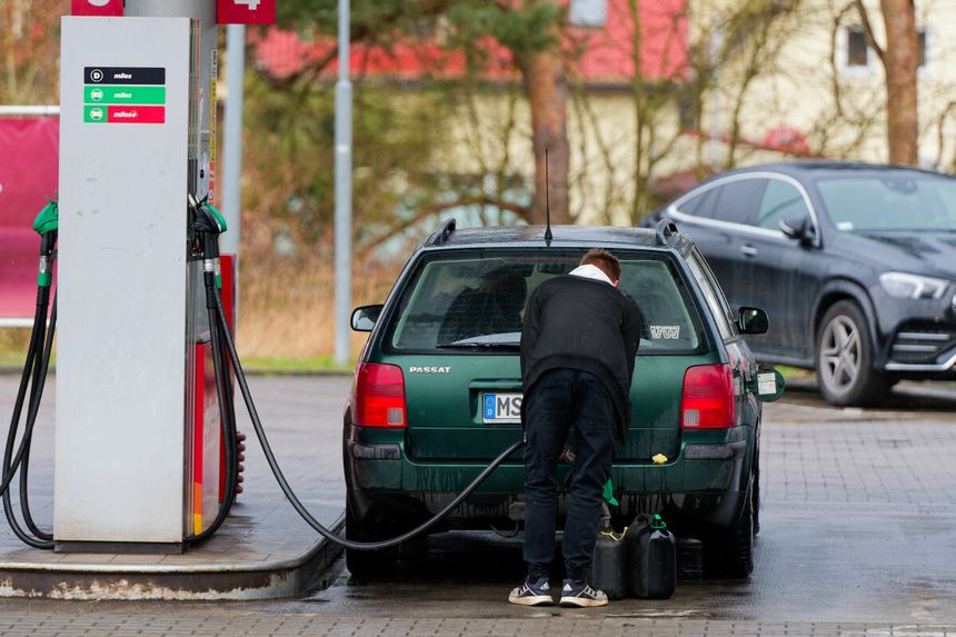 Mężczyzna tankuje zielony samochód osobowy na stacji benzynowej, obok stoi czarny SUV.