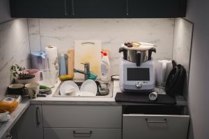 Zabałaganiona kuchnia z brudnymi naczyniami i sprzętem kuchennym na blacie.