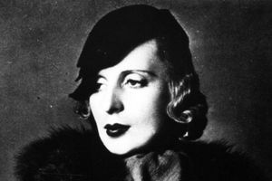 Kobieta z krótkimi, falującymi włosami, w eleganckim kapeluszu, z mocnym makijażem.