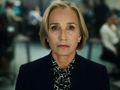 Kobieta z blond włosami i eleganckim strojem, patrząca w obiektyw, w tle biurowe wnętrze.