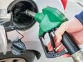 Ręka trzymająca zieloną pistolety do tankowania paliwa przy dystrybutorze.