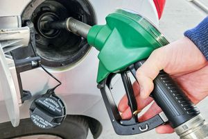 Ręka trzymająca zieloną pistolety do tankowania paliwa przy dystrybutorze.