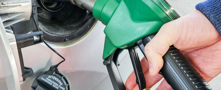 Ręka trzymająca zieloną pistolety do tankowania paliwa przy dystrybutorze.