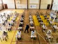 Uczniowie siedzą przy biurkach podczas egzaminu w sali gimnastycznej.