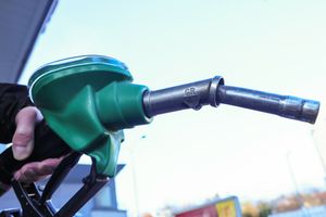 Zielona lanca do tankowania paliwa, trzymana w dłoni, na tle stacji benzynowej.