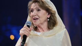 Na zdjęciu kobieta z mikrofonem, w jasnej chuście, śpiewa. Halina Frąckowiak.