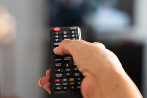Na zdjęciu widać rękę trzymającą pilot telewizyjny, wskazującą na ekran telewizora.