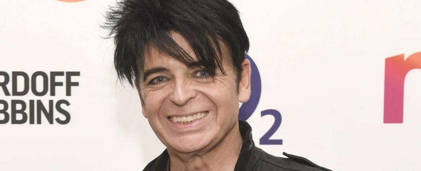 Mężczyzna z ciemnymi, roztrzepanymi włosami, uśmiechnięty, w czarnej skórzanej kurtce.