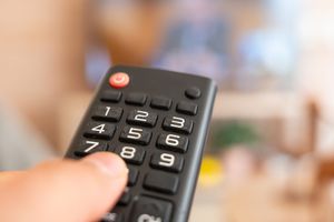 Pilot telewizyjny trzymany w dłoni, w tle nieostry obraz telewizora.
