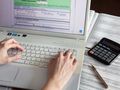 Osoba pracuje przy laptopie, wypełniając formularz podatkowy obok kalkulatora i dokumentów.