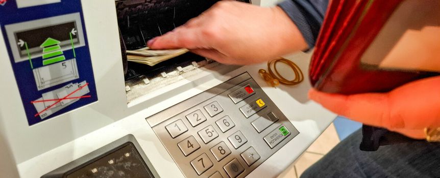 Osoba wypłaca pieniądze z bankomatu