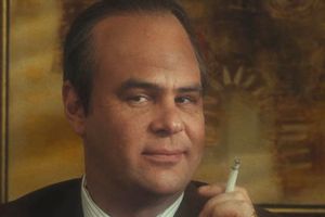 Mężczyzna z uśmiechem, trzymający papierosa, w garniturze.