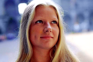 Młoda kobieta z długimi blond włosami, uśmiechająca się i patrząca w górę. Tło rozmyte.