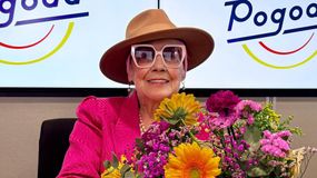 Kobieta w różowym kostiumie, w dużych okularach, trzyma bukiet kwiatów, w tle logo 