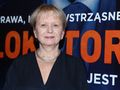 Na zdjęciu uśmiechnięta kobieta w ciemnej sukience, w tle widoczny duży napis: 