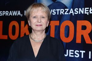 Na zdjęciu uśmiechnięta kobieta w ciemnej sukience, w tle widoczny duży napis: 