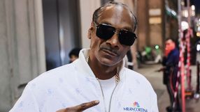 Na zdjęciu mężczyzna w ciemnych okularach, w białej bluzie, pokazujący znak pokoju.