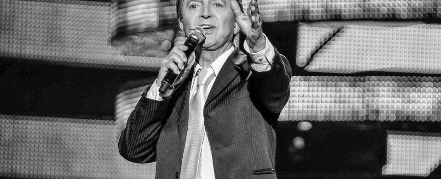 Na zdjęciu Jerzy Połomski. Mężczyzna w garniturze śpiewa do mikrofonu na scenie, z gestem wyrażającym emocje.