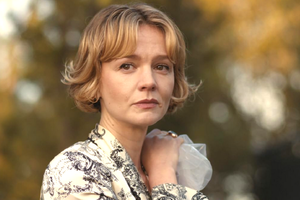 Na zdjęciu kobieta z krótkimi blond włosami, patrzy z niepokojem w tle drzew.