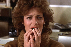 Kobieta w brązowym swetrze, ze łzami w oczach, trzyma się za twarz, wyglądając na przestraszoną.