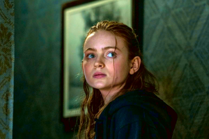 Młoda dziewczyna z długimi włosami patrzy w lewo, w tle zielona ściana i obraz w ramie.