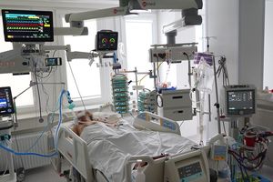 Szpitalna sala z pacjentem na łóżku, otoczonym sprzętem medycznym monitorującym.