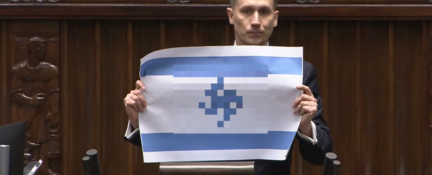 Konrad Berkowicz trzyma plakat z flagą, stojąc przy mównicy w sali obrad