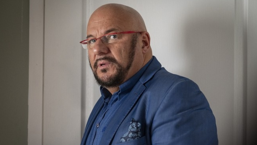 Mężczyzna w niebieskiej marynarce z brodą, patrzący w stronę kamery, o intensywnym wyrazie twarzy.