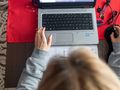 Osoba pracująca na laptopie przy biurku, z notesem i myszką obok. Czerwony obrus pod sprzętem.