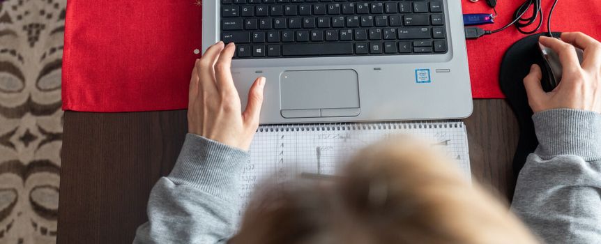 Osoba pracująca na laptopie przy biurku, z notesem i myszką obok. Czerwony obrus pod sprzętem.