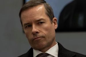 Mężczyzna w garniturze, z zamyśloną miną, patrzy w prawo.