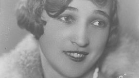 Kobieta z krótkimi, falującymi włosami, uśmiecha się, patrząc w stronę obiektywu. Czarno-biała fotografia.