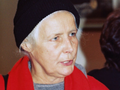 Agnieszka Osiecka w czarnej czapce i czerwonym płaszczu. W tle zarysy innych osób.