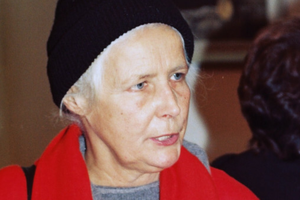 Agnieszka Osiecka w czarnej czapce i czerwonym płaszczu. W tle zarysy innych osób.