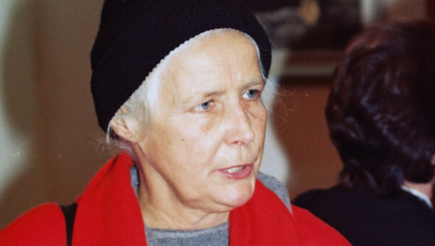 Agnieszka Osiecka w czarnej czapce i czerwonym płaszczu. W tle zarysy innych osób.