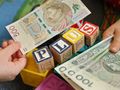 Dwie ręce trzymają banknoty obok kolorowych klocków, na których napisano „PLUS”.