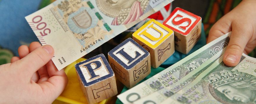 Dwie ręce trzymają banknoty obok kolorowych klocków, na których napisano „PLUS”.