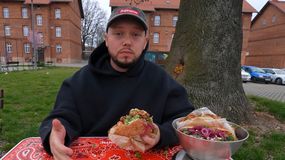 Książulo w czarnej bluzie siedzi przy stole, trzymając kebab.