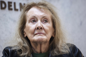 Kobieta z długimi, jasnymi włosami, patrzy w stronę kamery. Tło jednolite, lekko rozmyte.