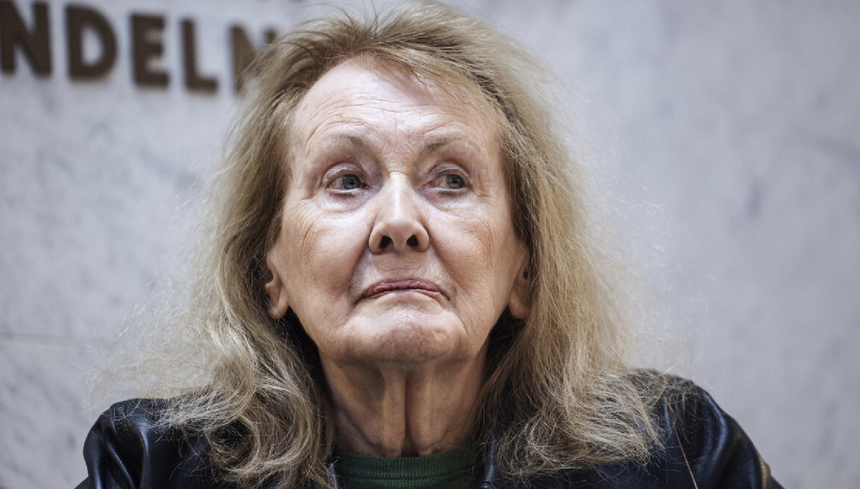 Kobieta z długimi, jasnymi włosami, patrzy w stronę kamery. Tło jednolite, lekko rozmyte.